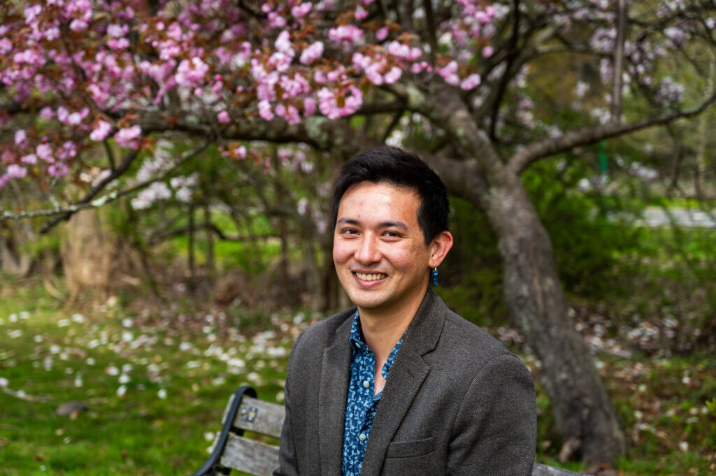 Professor Nathan Richbourg sitting on a bench with cherry blossom trees in the background